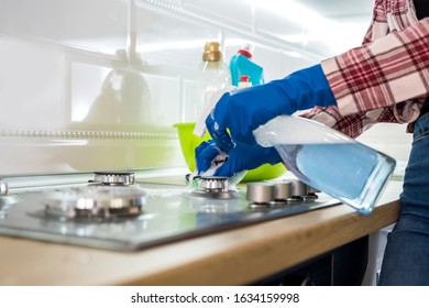 Woman Cleaning Stainless Steel Gas Surface In The Kitchen With Rubber Gloves.