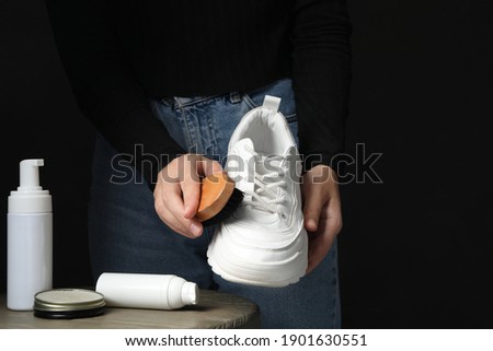 Woman cleaning stylish footwear at table against black background, closeup. Shoe care accessories