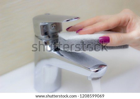 Woman cleaning tap with sponge in bathroom, close-up