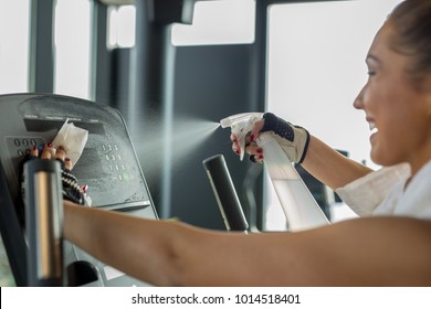 Woman cleaning work out area at the gym while smiling - Powered by Shutterstock