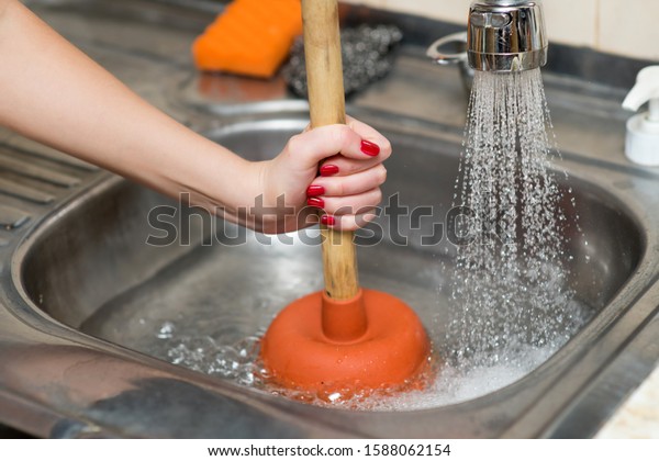 woman cleans\
plunger with clogged sink, close\
up
