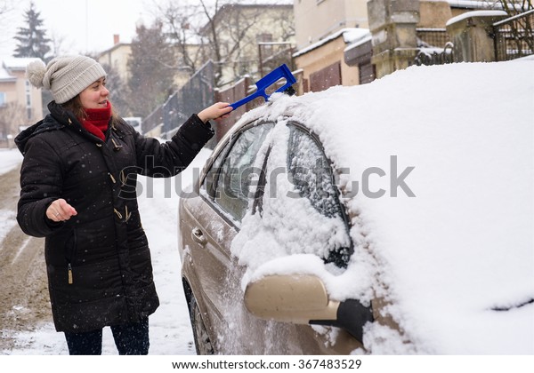 Woman\
cleans snow car outdoor during storm winter\
weather