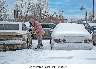 A Woman Cleans Snow From Her Car In The Parking Lot In Inclement Weather