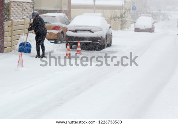 Woman\
cleans street from snow. Winter weather background\
