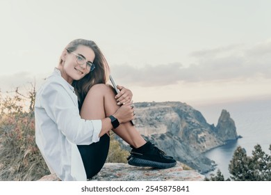 Woman, Cliff, Sunset - Smiling Woman Sitting on Clifftop at Sunset with Ocean View. - Powered by Shutterstock