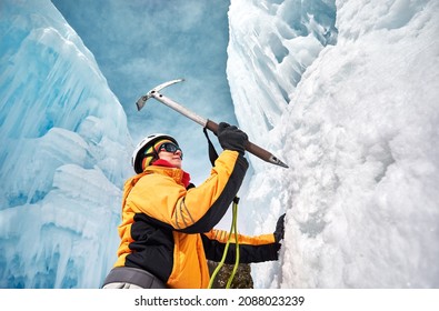 Woman is climbing frozen waterfall with ice axe in orange jacket in the mountains. Sport mountaineering and alpinism concept.