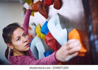 Woman climbing indoor rock wall focusing on grip and technique during training session in climbing gym - Powered by Shutterstock