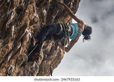 A woman is climbing a rock wall with a green rope. Concept of adventure and determination as the woman faces the challenge of scaling the steep rock face - Powered by Shutterstock