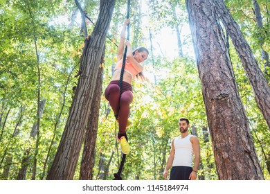 Woman Climbing Rope Tied To A Tree For Better Fitness In Outdoor Gym