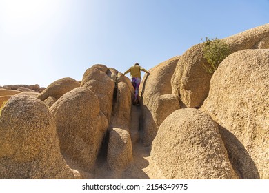 Woman Climbing Through A Channel Of Rocks In The Desert