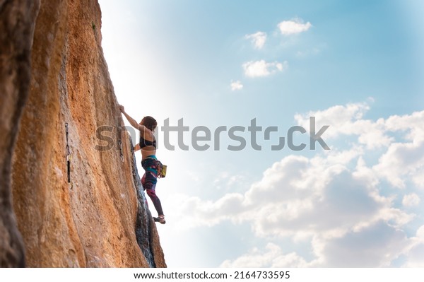 A woman climbs\
a rock against a blue sky, a strong girl trains strength and\
endurance, an extreme sport, rock climbing on natural terrain, a\
rock climber climbs with a\
rope