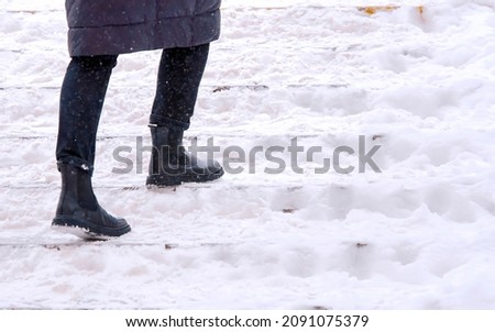 Woman climbs snow covered staircase. Person climbing slippery snowy stairs. Female walks up stairs with snow steps during snowfall. Dangerous winter walking. Selective Focus