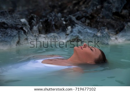 A woman with closed eyes floats in blue lagoon spa resort Blue Lagoon in Iceland, her red hair is around the head