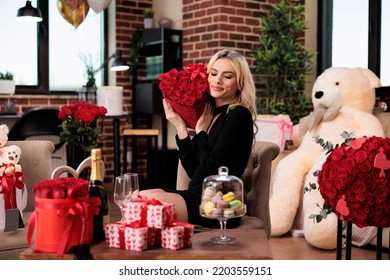 Woman With Closed Eyes Holding Red Roses Heart Shaped Box, Receiving Luxury Valentines Day Presents. Young Blonde Girl Sitting In Living Room With Bear Soft Toy, Flowers Bouquet Gifts