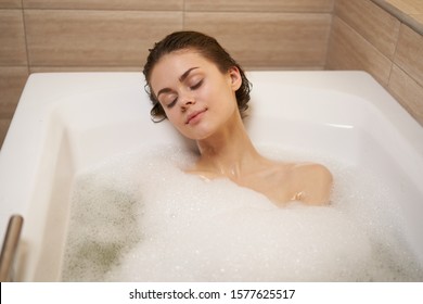 A woman with closed eyes lies in the bathtub with white foam - Powered by Shutterstock