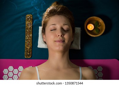 Woman with closed eyes Relaxing at home, lying on acupuncture mat. Candles and incense aroma sticks.