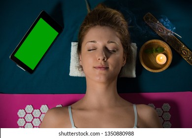 Woman with closed eyes Relaxing at home, lying on acupuncture mat. Candles and incense aroma sticks. Digital tablet with empty green screen