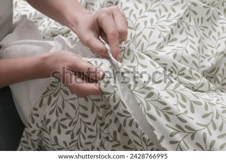 Woman is closing buttons on duvet cover while making the bed, close up	