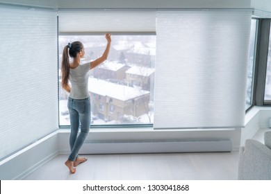 Woman closing cellular shades on apartment window keeping energy and heat indoors with honeycomb blind curtain. Cordless pleated shades in modern home living lifestyle. Interior decor design.