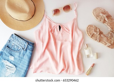 Woman clothes and accessories: pink top, jeans skirt, perfume, sandals, sunglasses, hat, lipstick on white background. Flat lay trendy fashion feminine background. Fashion beauty background.