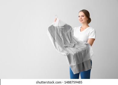 Woman with clothes after dry-cleaning on light background