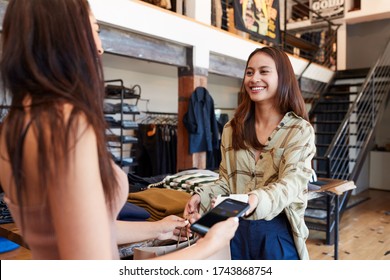 Woman In Clothing Store Making Contactless Payment With App On Mobile Phone