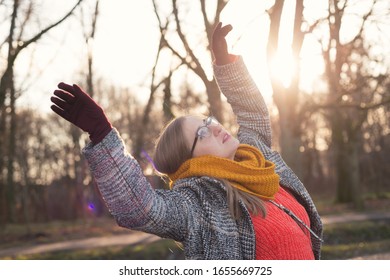 Woman in a coat and glasses dancing in the park in autumn