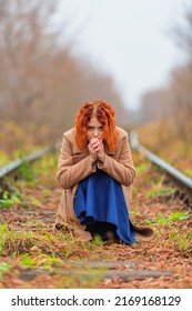 Woman in coat sitting on railway path in prayer pose in autumn day. Shallow dof