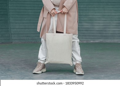 Woman in coat with white cotton bag in her hands. Mockup and zero waste concept. Cropped.