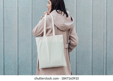 Woman In Coat With White Cotton Bag In Her Hands. Mockup And Zero Waste Concept. Cropped.