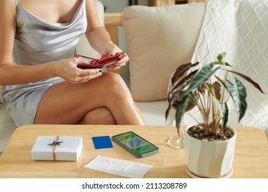 Woman In Cocktail Dress Checking Money In Wallet And QR Code On Smartphone Before Leaving Home For Party