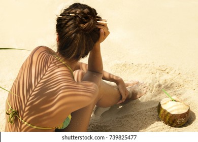 Woman with coconut drink under palm leaf on the beach