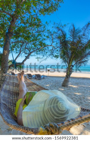 woman with coconut in a hammock on a paradise beach under palm trees