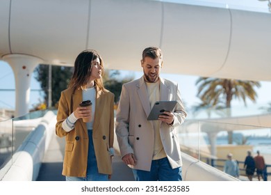 Woman with coffee cup to go and man with digital tablet device walking on a sunny day. Stylish couple spending time outside, walking, drinking coffee, using tablet. - Powered by Shutterstock