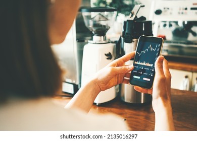 Woman In Coffee Shop With Mobile Investing App In Her Hand, Close-up