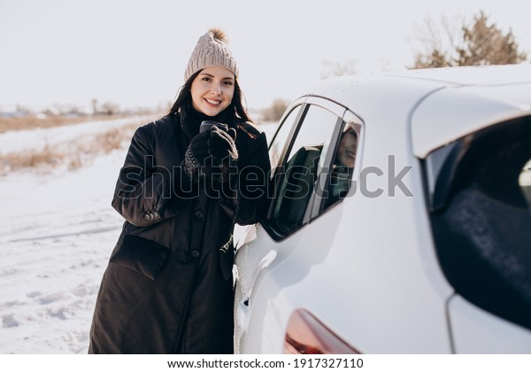 Woman with
coffee standing by car in a winter
field