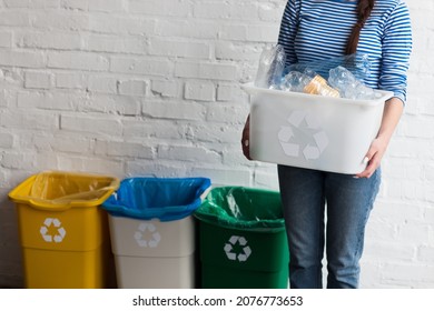 Una mujer recolectando basura y sosteniendo una papelera de reciclaje con botellas de plástico al aire libre