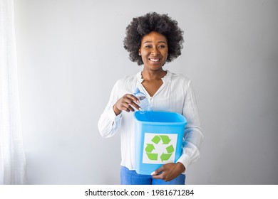 A Woman Collecting And Separating Recyclable Garbage Plastic Bottles Into A Trash Bin At Home. African American Woman Holding Recycling Plastic Bottles Smiling With A Happy And Cool Smile On Face. 