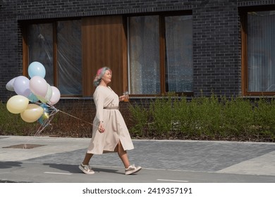 Woman in colored hair walks with an armful of balloons and drinks a refreshing beverage - Powered by Shutterstock