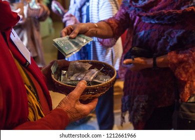 Woman with colorful clothes is putting 10 canadian dollars into a basket as voluntary contribution after a show - Closeup picture with a man in red shirt holding the basket
