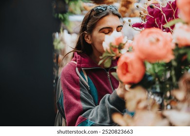 A woman in a colorful jacket smells flowers, capturing a moment of tranquility and appreciation for nature. - Powered by Shutterstock