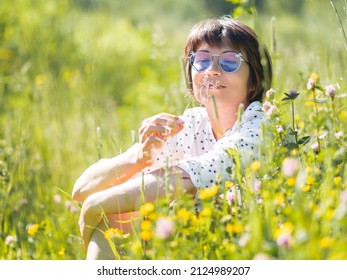 Woman in colorful sunglasses, enjoys sunlight and flower fragrance on grass field. Summer vibes. Relax outdoors. Self-soothing. - Shutterstock ID 2124989207