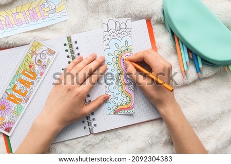Woman coloring bookmark on bed