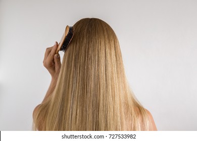 Woman with comb brushing her dry blonde hair on the gray background. Cares about a healthy and clean hair. Beauty salon concept. 