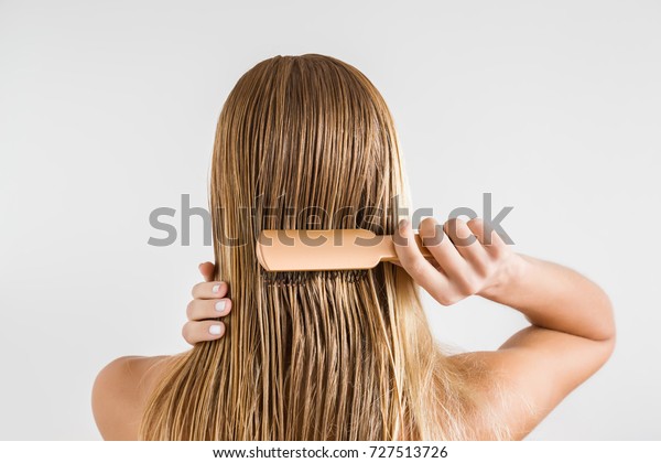 Woman with comb brushing her wet blonde hair\
after shower on the gray background. Cares about a healthy and\
clean hair. Beauty salon concept.\
