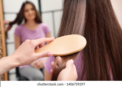 Woman combing friend's hair with cushion brush indoors, closeup