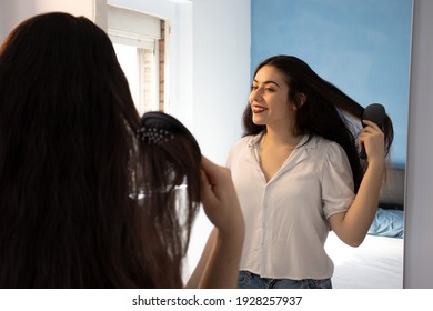 Woman combing her hair and smiling in front of the mirror. - Shutterstock ID 1928257937
