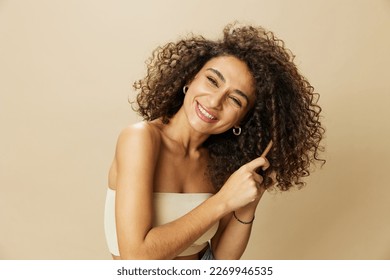 Woman combs curly afro hair with wooden comb, home beauty care styling products, hair loss after covid-19, smile on beige background - Powered by Shutterstock