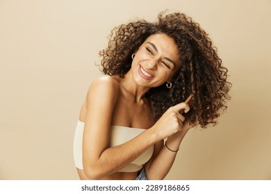 Woman combs curly afro hair with wooden comb, home beauty care styling products, hair loss after covid-19, smile on beige background - Powered by Shutterstock