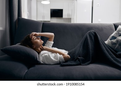 a woman in a comfortable room lies on a sofa covered with a gray blanket